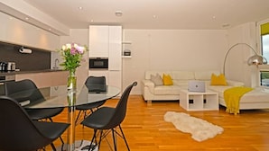 A modern living room with a dining area, white sofas, and a laptop on a side table. - Penthouse Kew (Brentford)