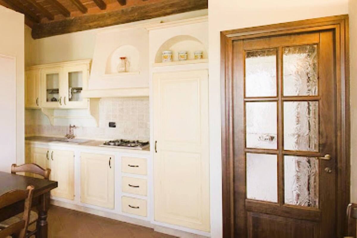 Una cocina con armarios blancos, una mesa de comedor de madera y un televisor.