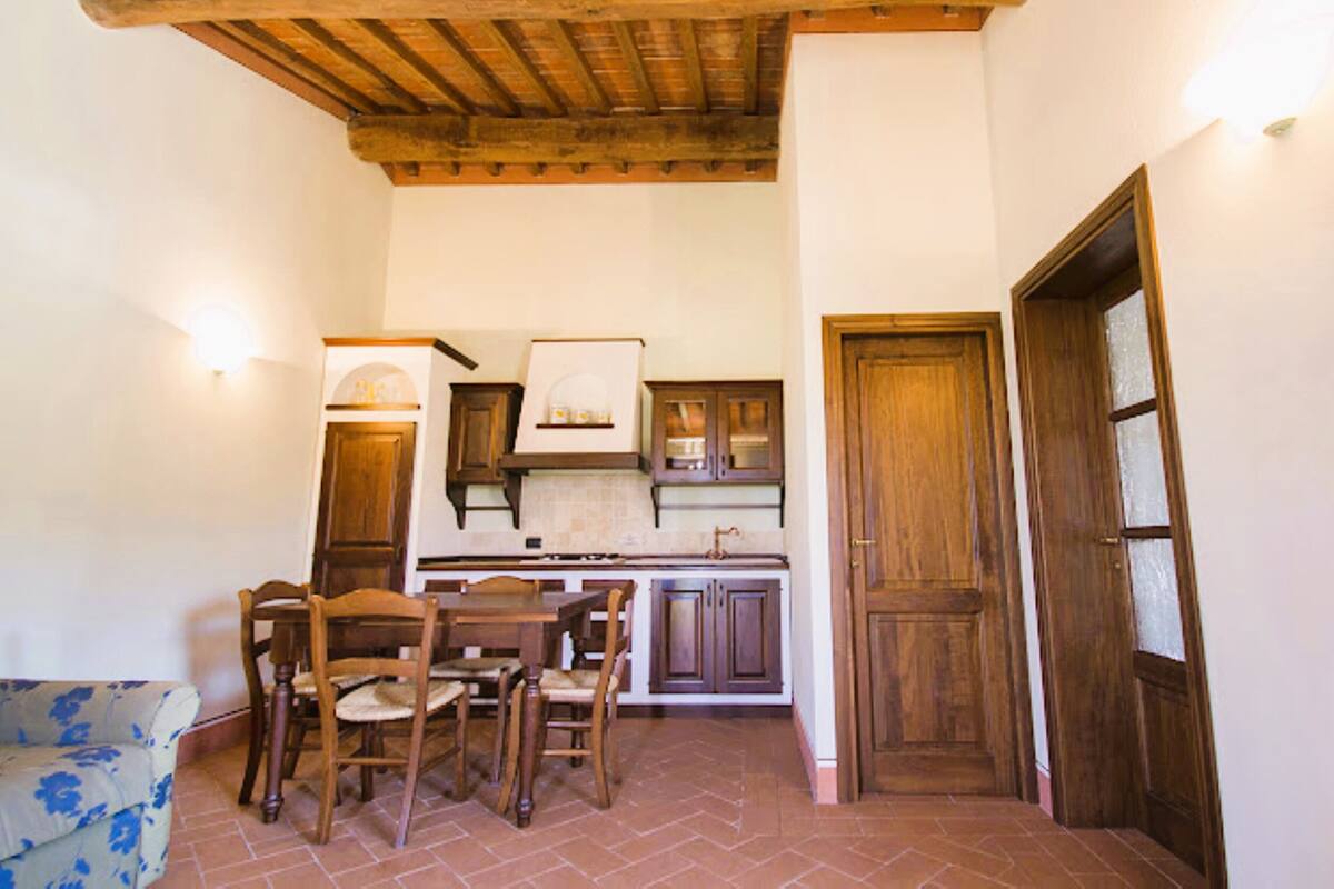 Una cocina compacta con armarios de madera, una mesa de comedor con sillas y suelo de baldosas.