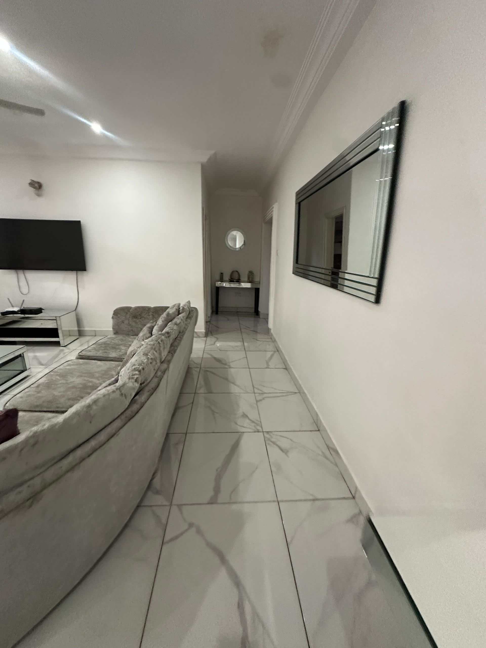 A modern living room with a sofa, a flat-screen TV, a console table, and a mirror.