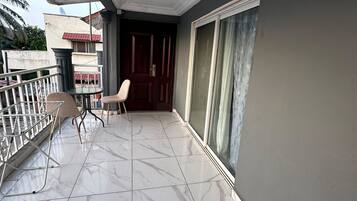 A balcony with a tiled floor, a chair, a small table, and a door leading to an interior room.