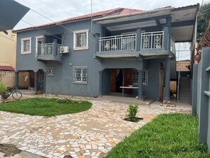 A two-story residential building with a tiled patio, a small lawn, and a staircase leading to the upper floor. - Luxury Spacious two bedroom apartment for comfortable living. Well furnished . (Banjul)