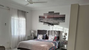 Une chambre à coucher moderne avec un lit, un ventilateur de plafond, une table de chevet, une lampe et une vue sur l’océan.