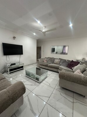 Una sala de estar moderna con un televisor de pantalla plana, una mesa de centro de vidrio, dos sofás, un ventilador de techo y un espejo grande.