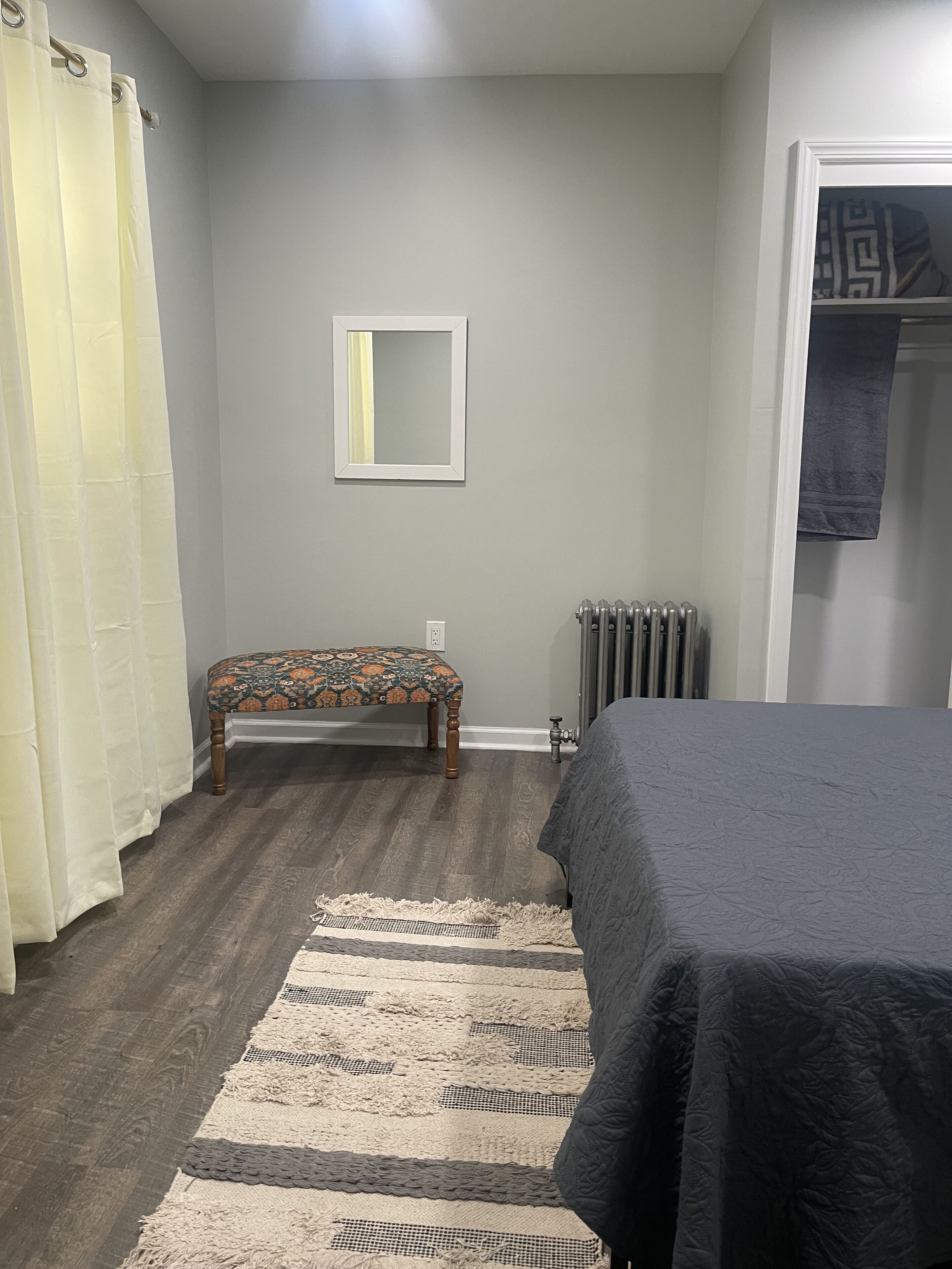 A bedroom with a bed, a bench, a radiator, and a mirror on the wall.