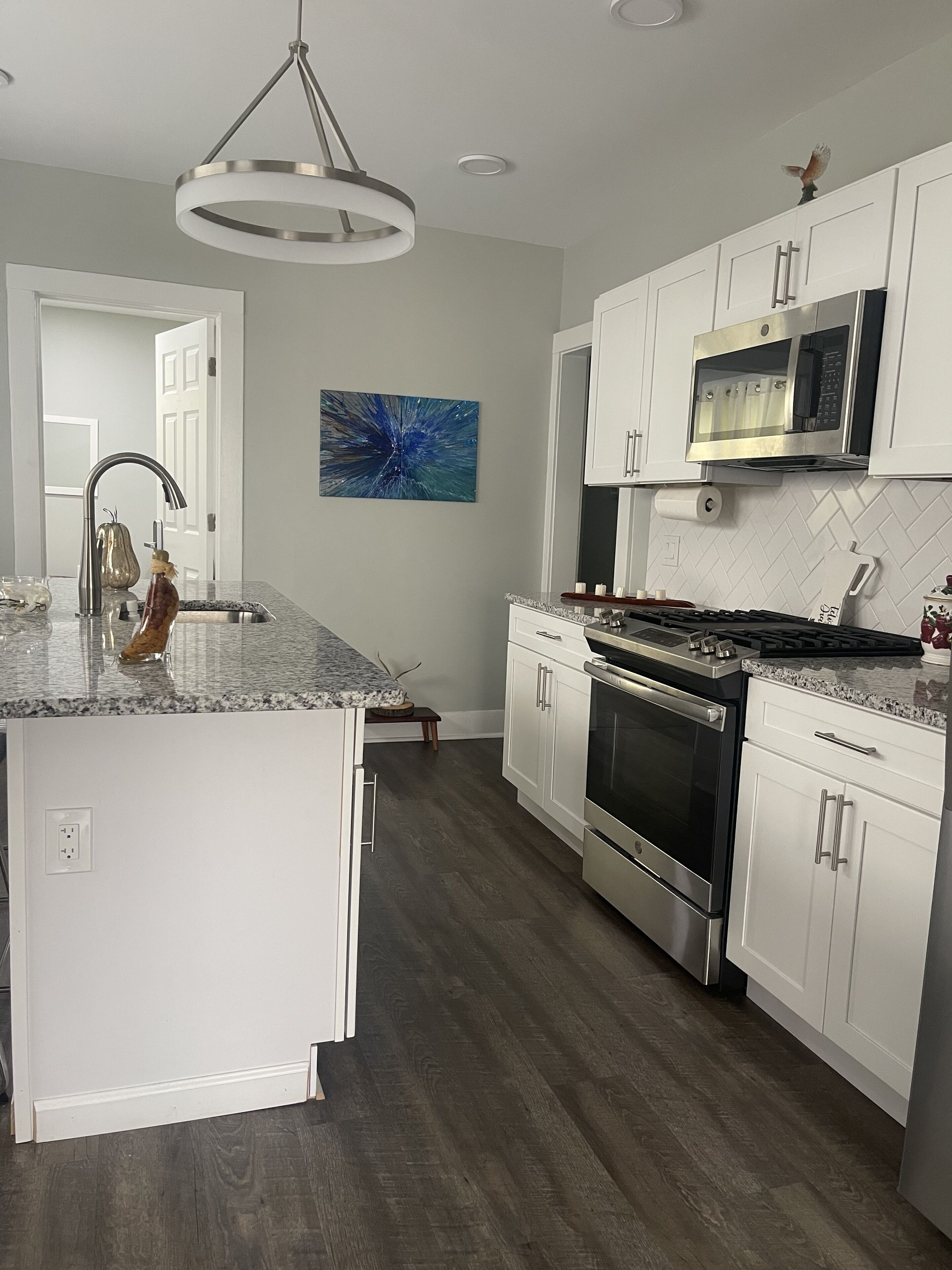 A modern kitchen with white cabinetry, a central island, stainless steel appliances, and a contemporary pendant light.