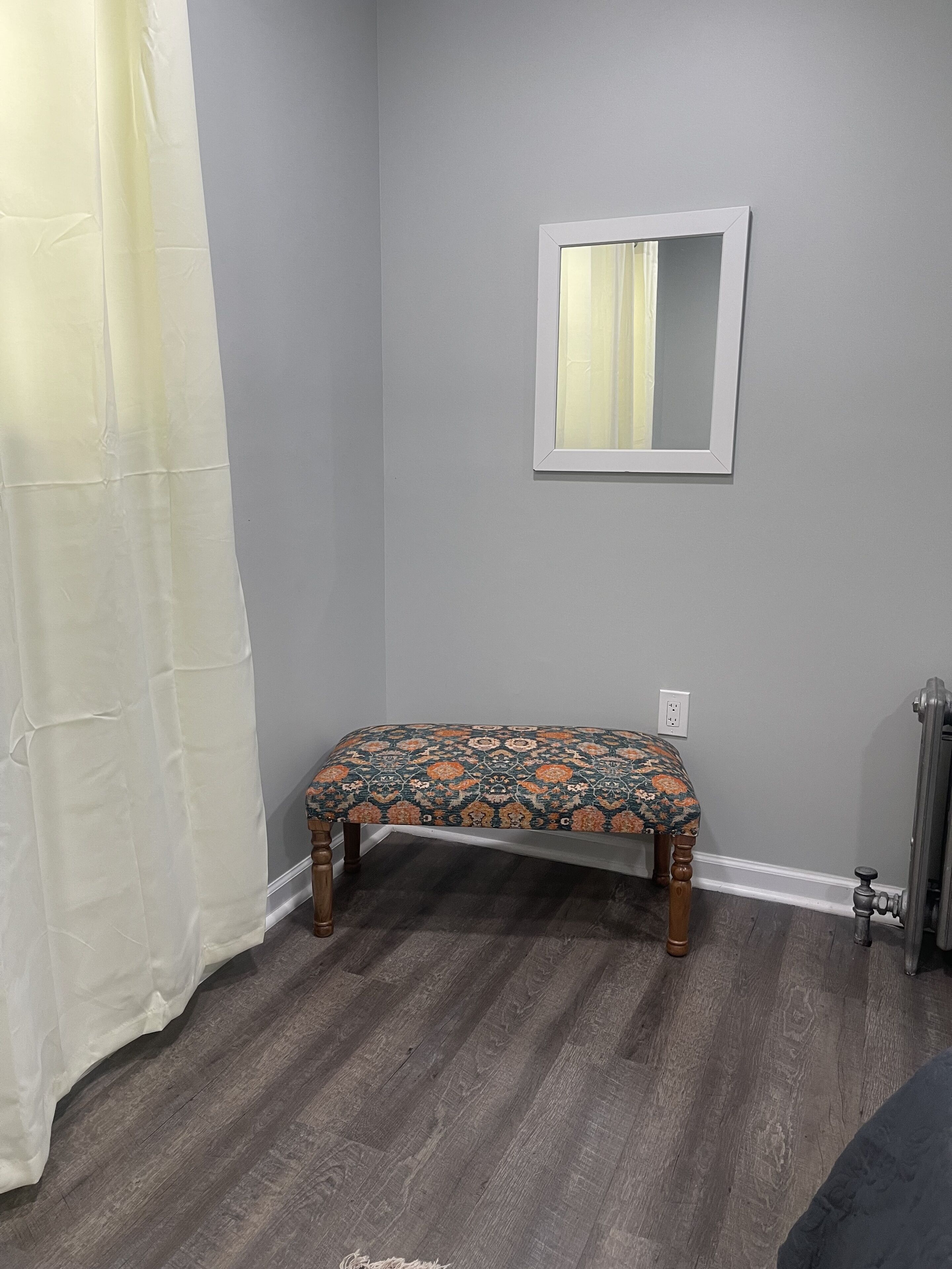 A bathroom with a bench, a mirror, and a radiator.