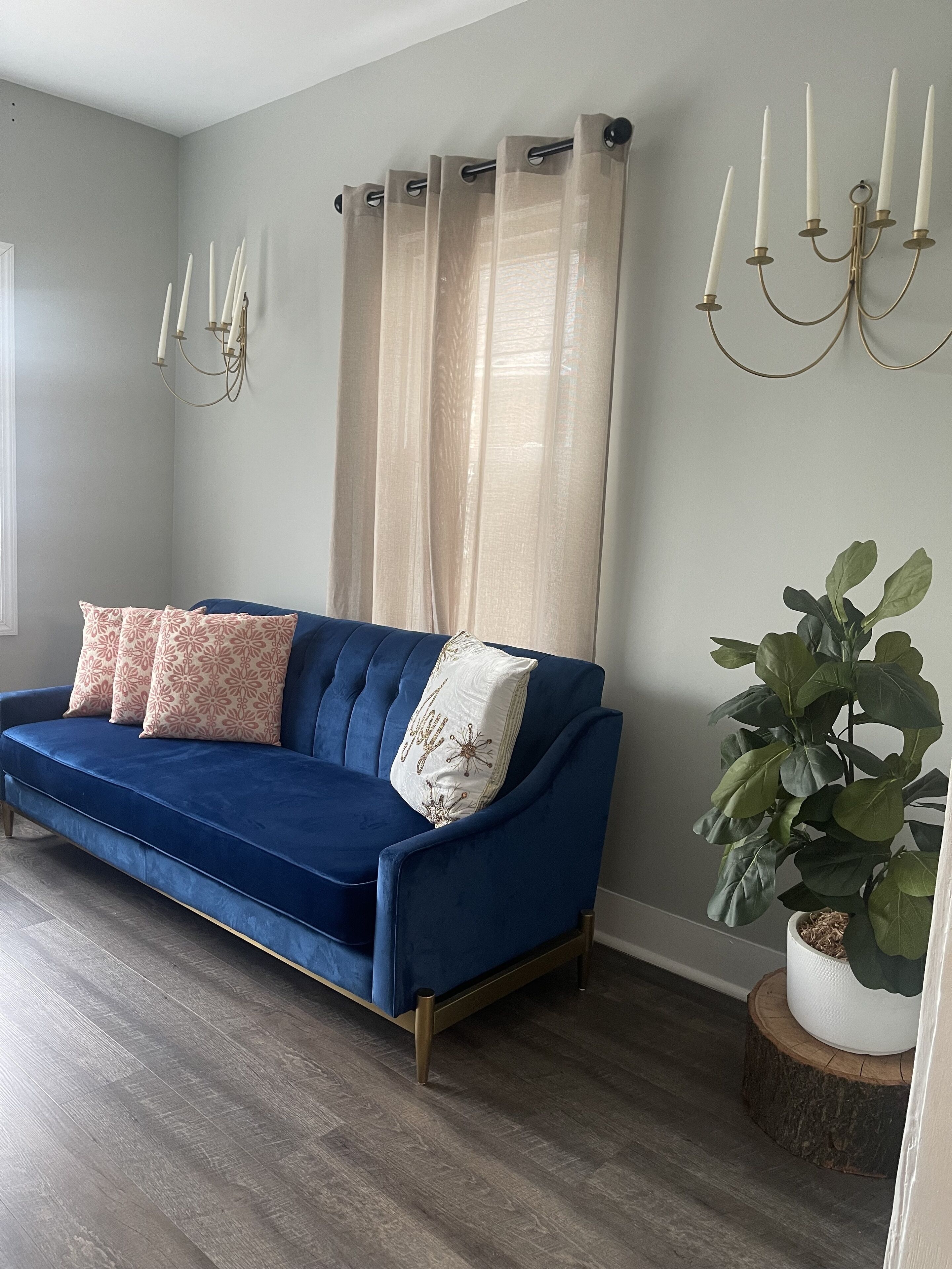 Un canapé bleu agrémenté de coussins à motifs, une plante en pot et un chandelier posés sur un plancher en bois.