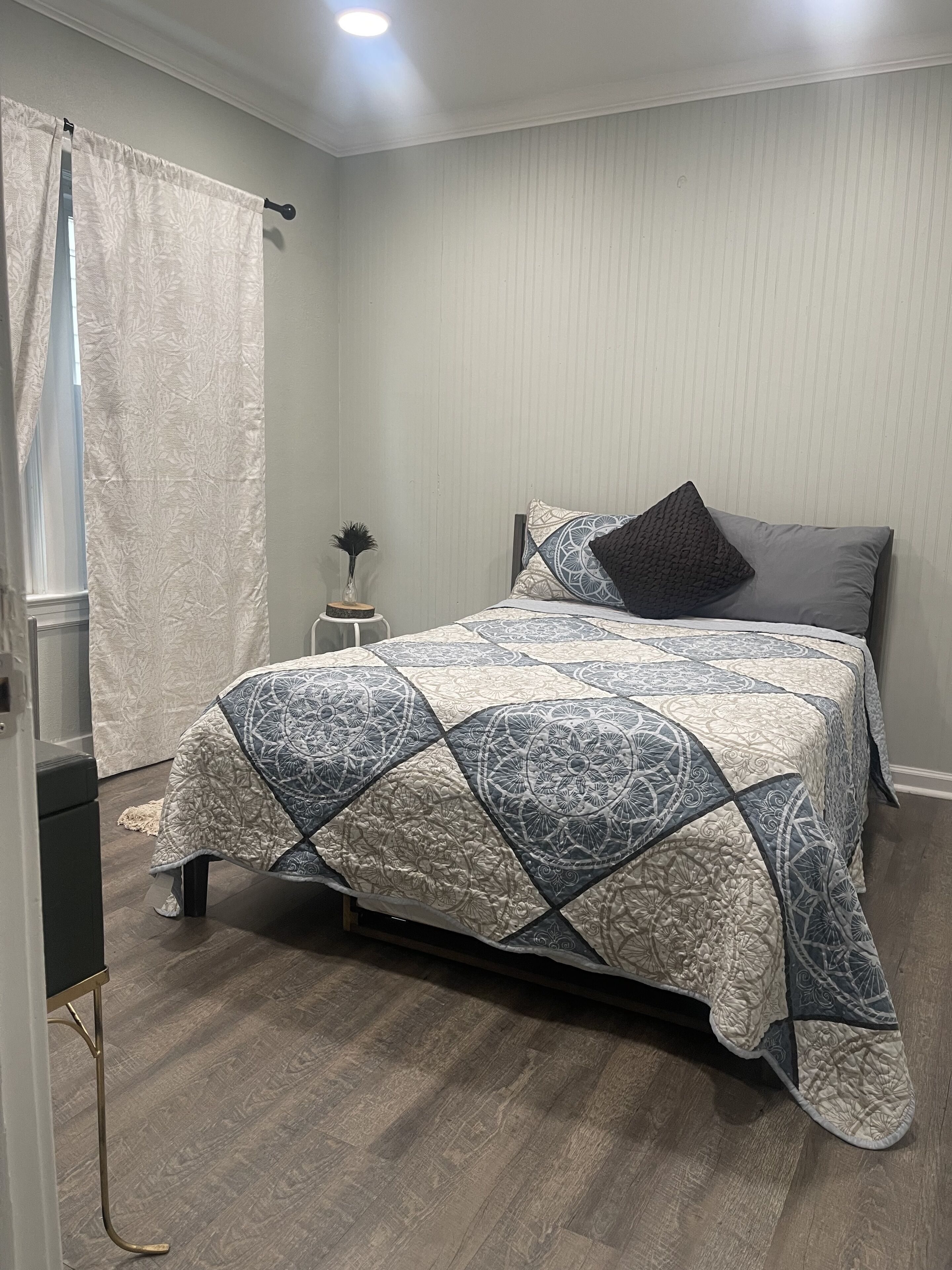 A bedroom with a bed, a nightstand, a lamp, and a window with curtains.