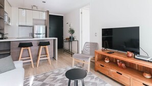 A modern kitchen with a dining area, a TV, and a seating arrangement. - Boho Apartment - Pool, Parking & Mall. (Las Condes)