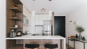 A modern kitchen with white cabinets, a stainless steel refrigerator, and two black bar stools. - Boho Apartment - Pool, Parking & Mall. (Las Condes)