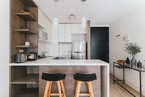 A modern kitchen with white cabinets, a stainless steel refrigerator, and a bar area with stools. - Boho Apartment - Pool, Parking & Mall. (Las Condes)