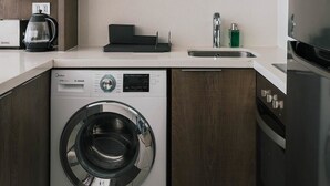 A compact kitchen with a washing machine, a microwave, and a sink. - Boho Apartment - Pool, Parking & Mall. (Las Condes)