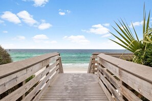 A wooden boardwalk leading to a beach with clear blue water and a calm sea.