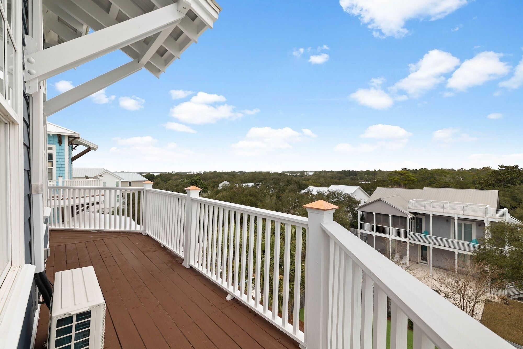 A wooden deck with white railings, overlooking a residential area with houses and greenery.