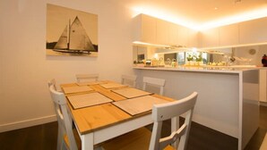 Una cuina moderna amb armaris blancs, una taula de dinar de fusta amb cadires, i un quadre d'un veler a la paret.