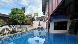 Una piscina con diseño de baldosas a cuadros, rodeada por una valla blanca y un edificio de fachada roja.