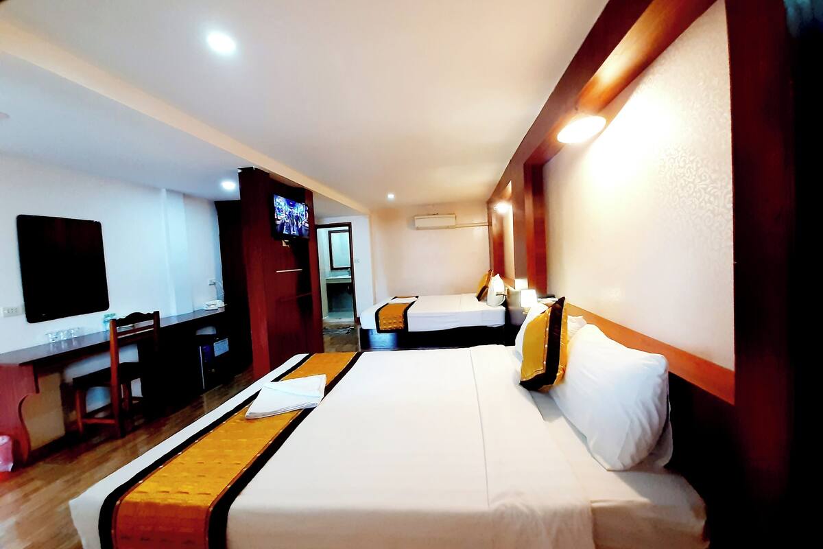A hotel room with two beds, a desk, a TV, and a mirror.