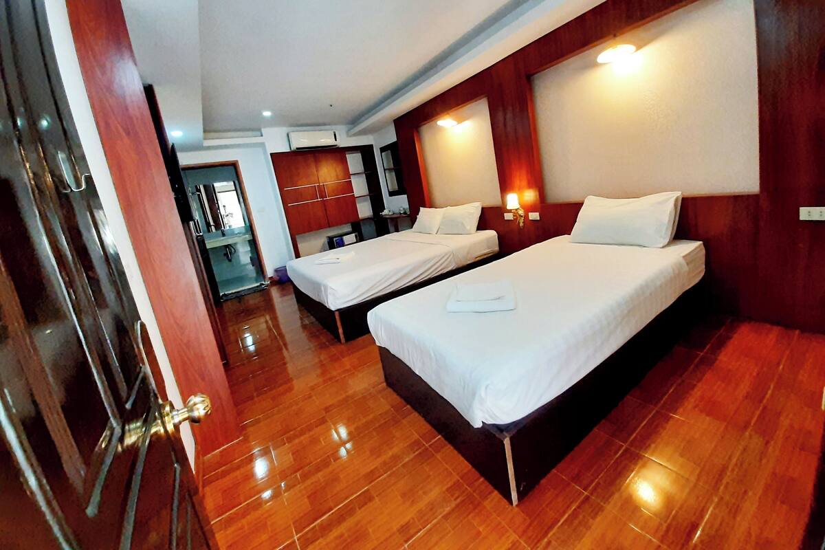 A hotel room with two beds, wooden flooring, and a wooden wardrobe.