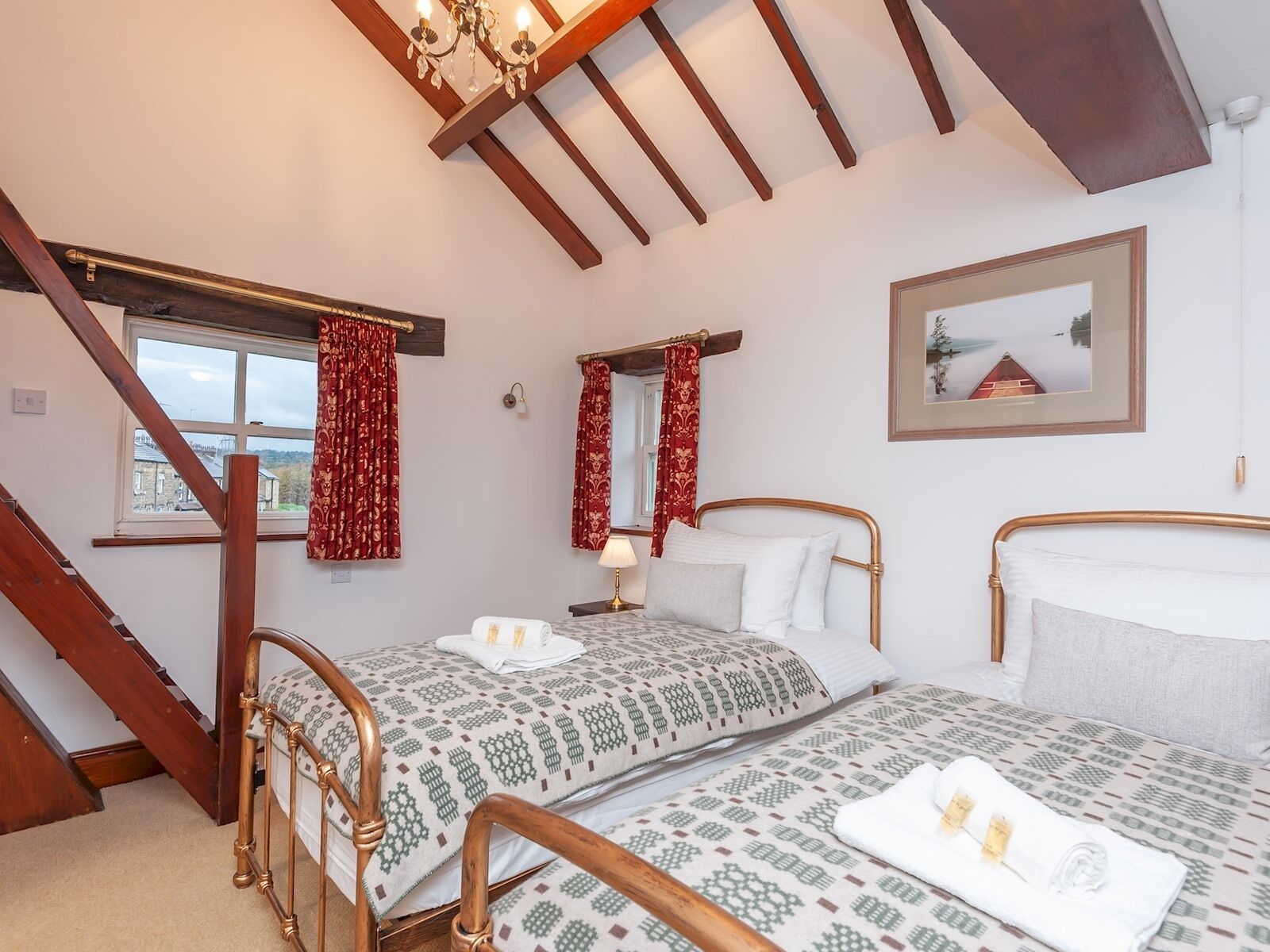 Quarto com duas camas, escada de madeira, um candelabro e um quadro na parede.