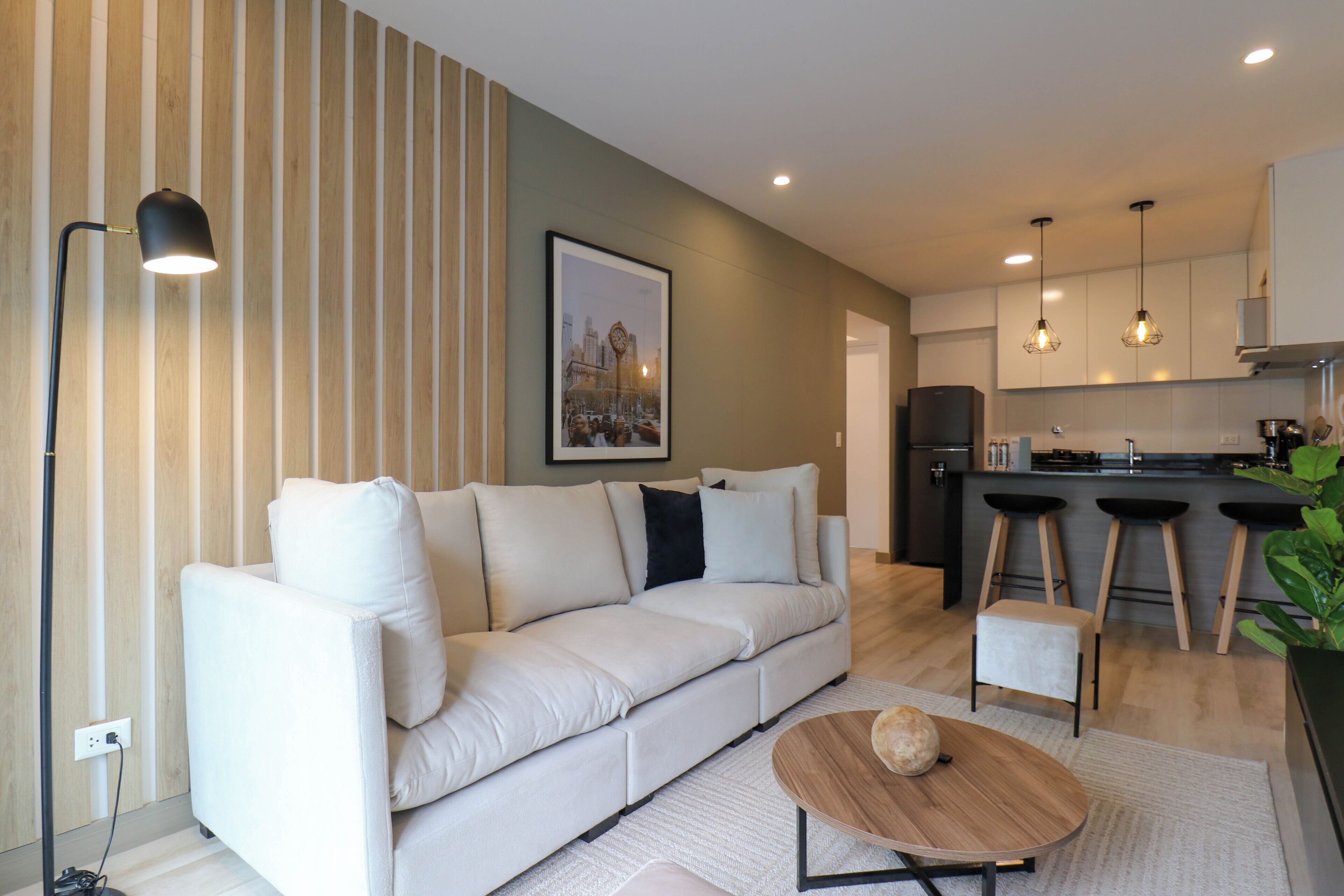 A modern living room with a sofa, a coffee table, and a kitchen area with bar stools.