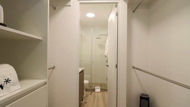 Un pasillo estrecho que conduce a un baño con inodoro, ducha y perchero.