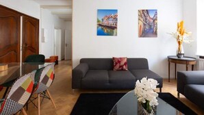 En moderne stue med en mørk sofa, et glasbord og et spiseområde med et træbord og farverige stole.