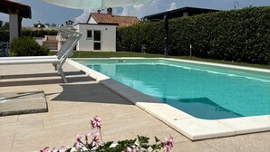 En swimmingpool med hvid parasol, liggestol og en potteplante med lyserøde blomster.