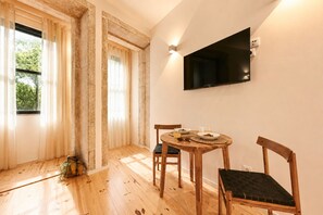 A room with a wooden dining table, chairs, a TV mounted on the wall, and a window with curtains. - FindMe inPorto Bonfim (Porto)