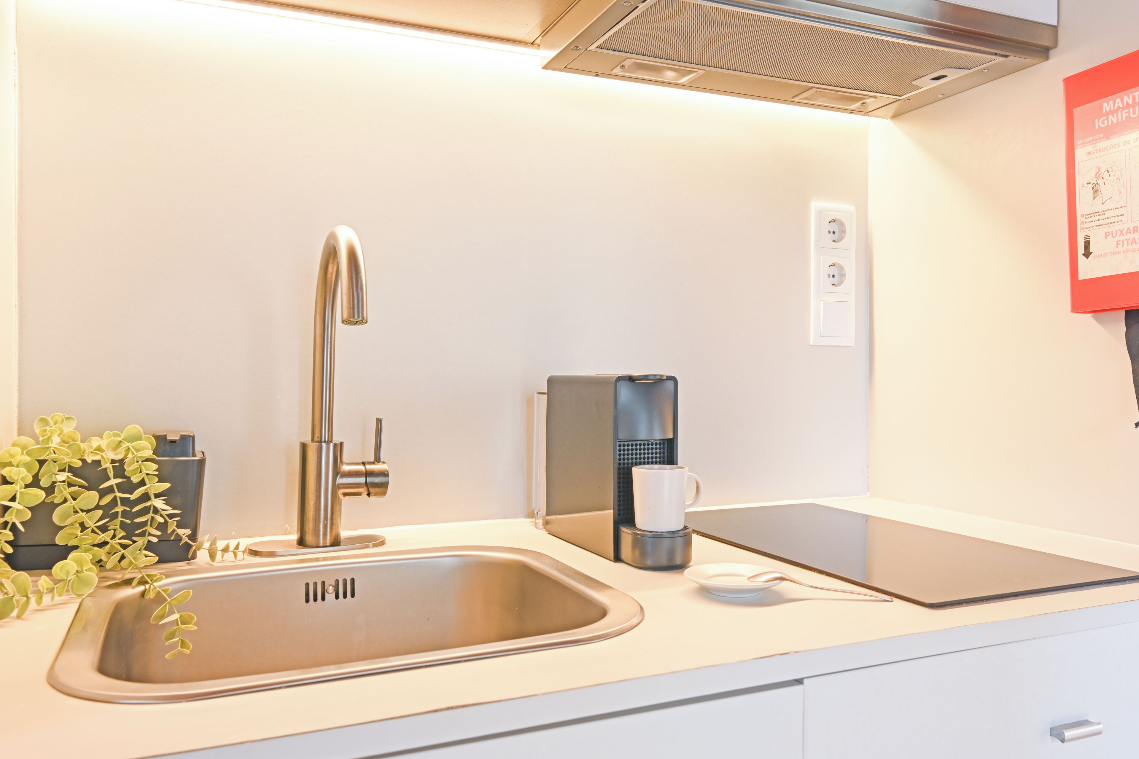 Una cocina moderna con un lavamanos de acero inoxidable, una cafetera y una tableta sobre la encimera.
