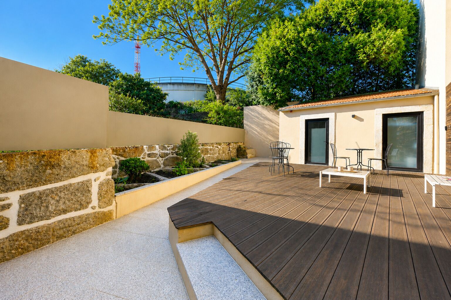 Eine Terrasse mit Holzboden, Steinmauern und einer kleinen Sitzecke mit Tischen und Stühlen.