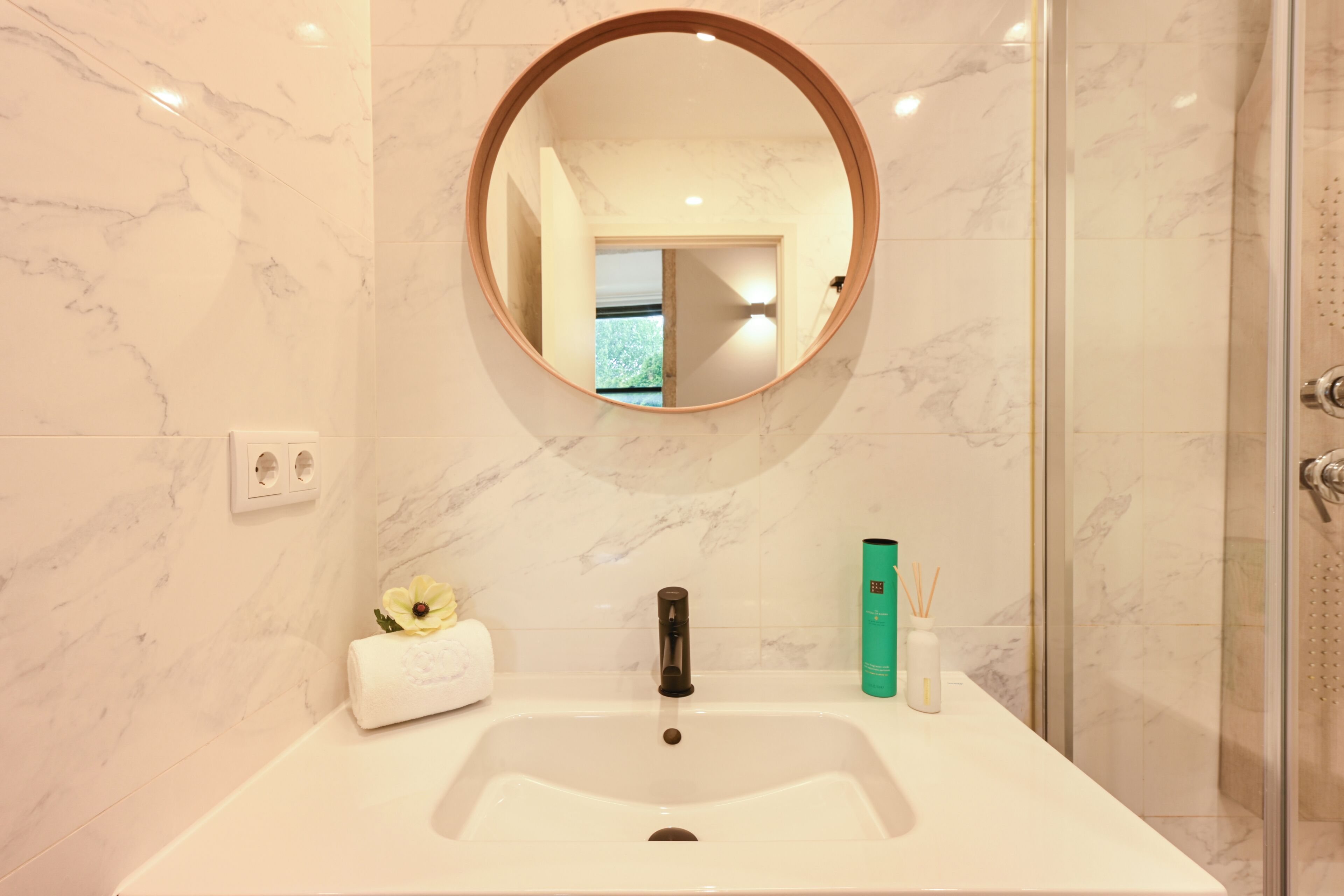 A bathroom with a marble sink, a round mirror, a towel, and a green bottle.