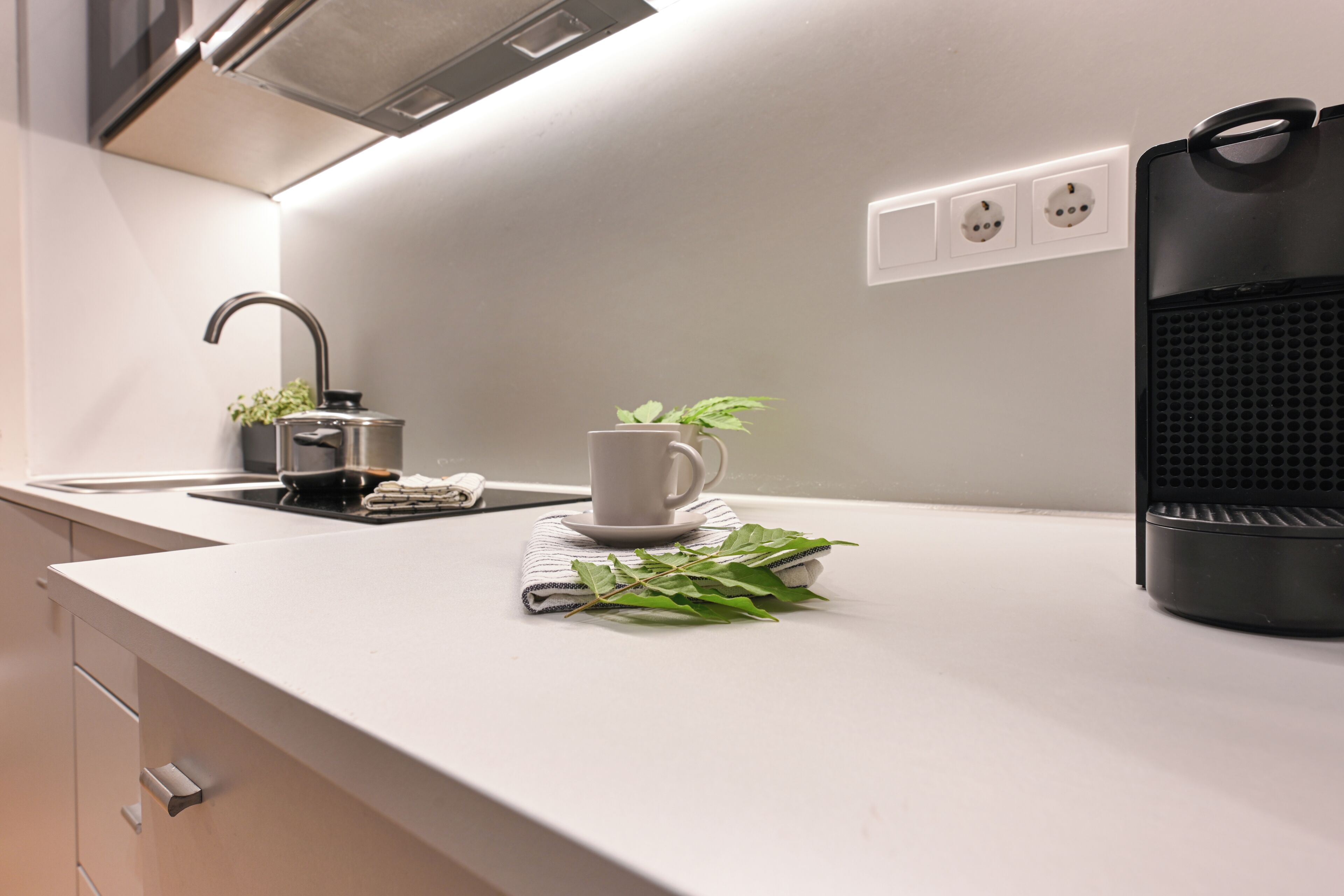 Une cuisine moderne avec un plan de travail blanc, une bouilloire, une tasse et une plante.