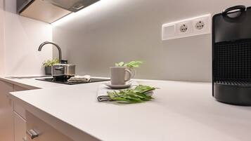 Une cuisine moderne avec un plan de travail blanc, une bouilloire, une tasse et une plante.