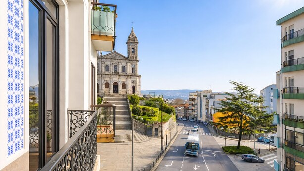 A street view with a building featuring a bell tower, a staircase leading to a balcony, and a clear road with vehicles. - FindMe inPorto Bonfim (Porto)