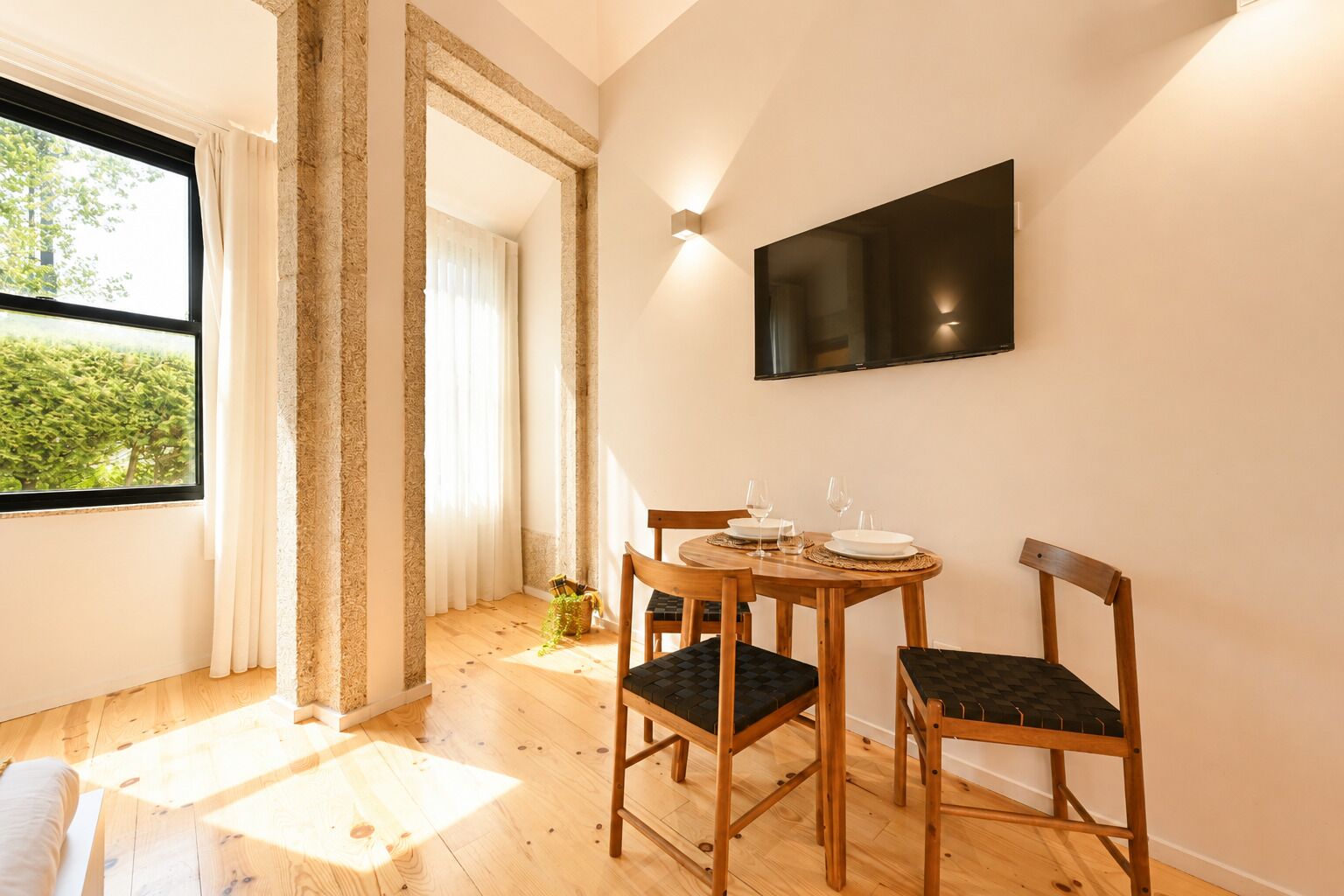 Un comedor con una mesa redonda de madera, cuatro sillas y un televisor de pantalla plana montado en la pared.