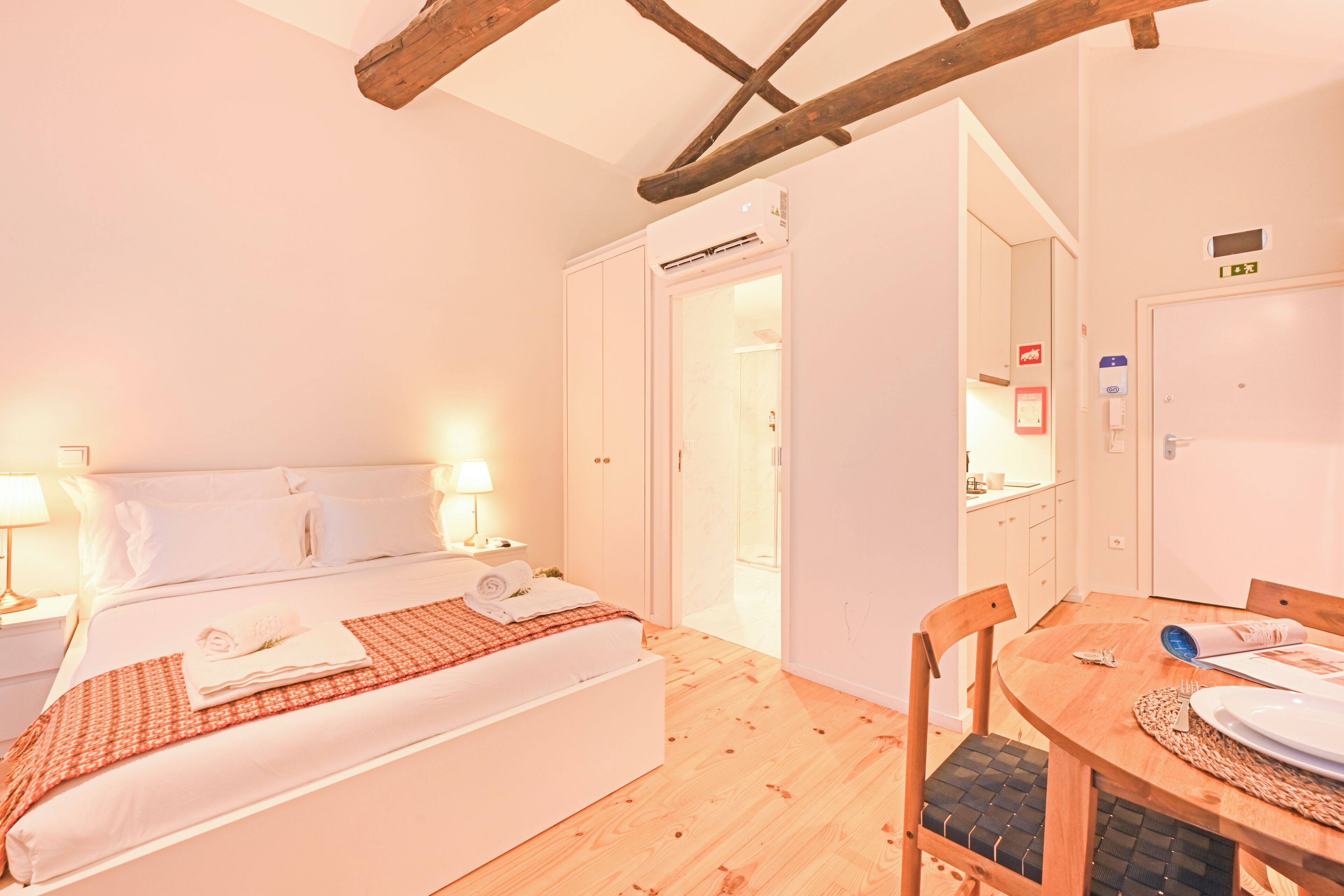 A bedroom with a bed, bedside lamps, a wooden dining table, and a chair.