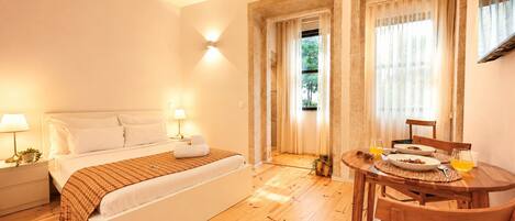Un dormitorio con cama, lámparas de noche, suelo de madera, una mesa de comedor con sillas y una ventana con cortinas.