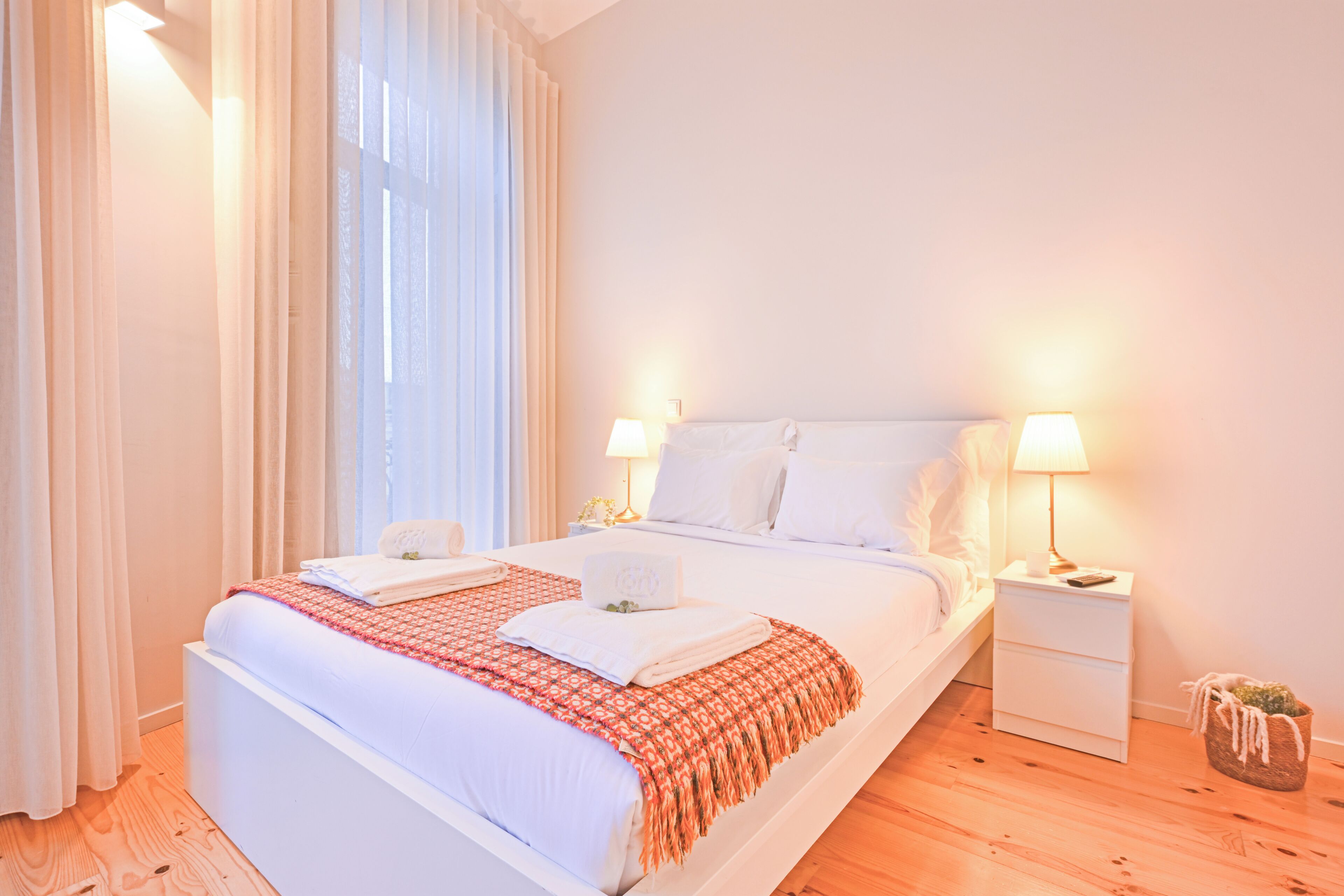 A hotel room with a large bed, two bedside tables, a nightstand, and a window with curtains.
