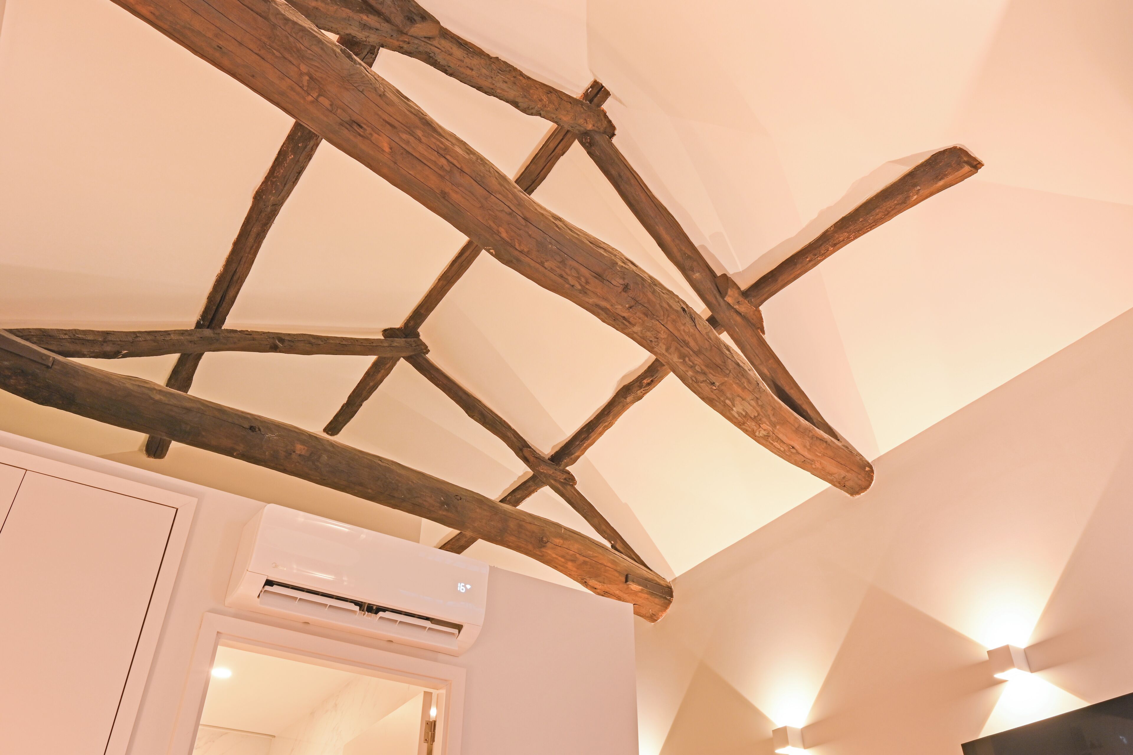 A room with exposed wooden beams, an air conditioning unit, and a white door.
