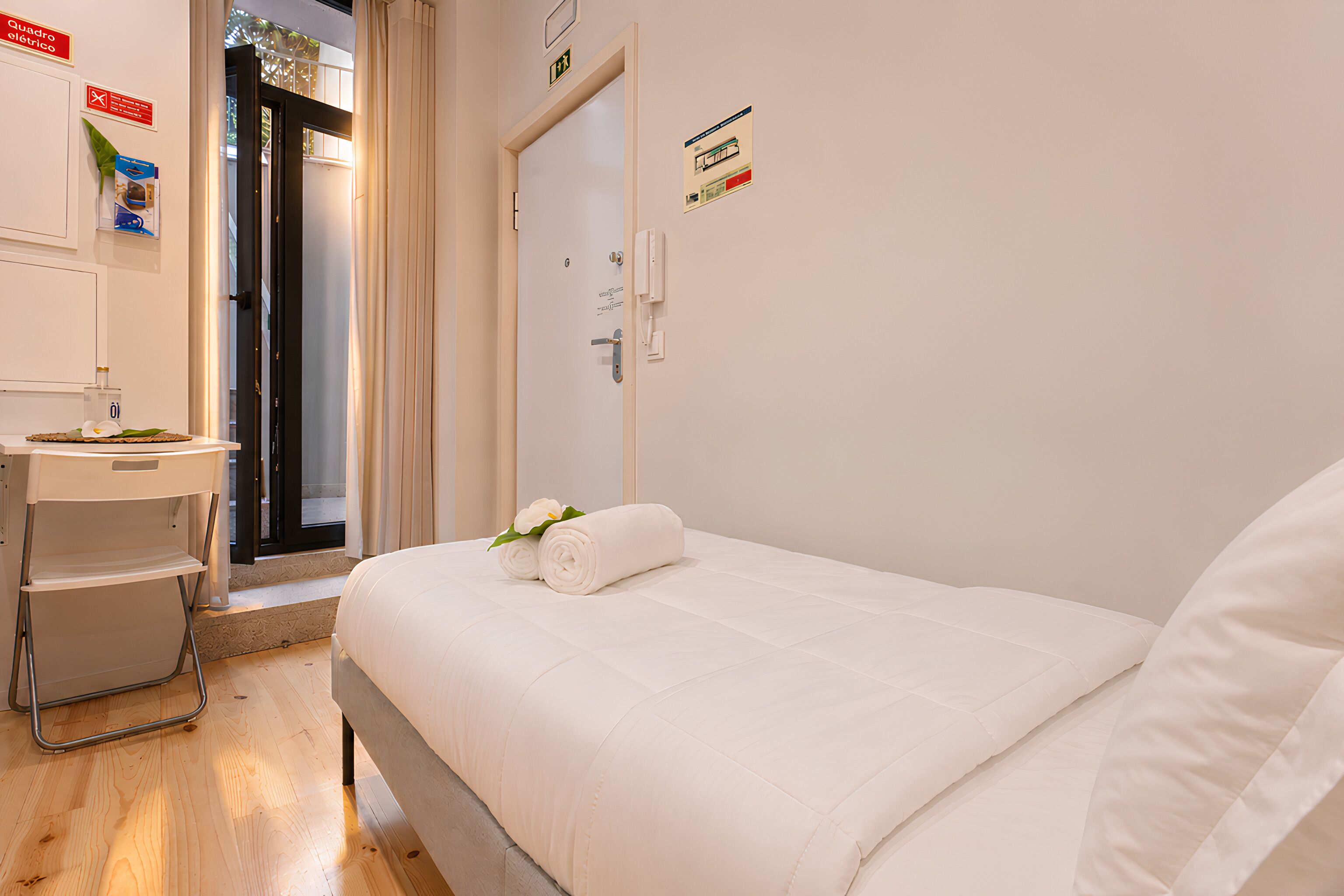 A hotel room with a bed, a desk, a chair, and a door.