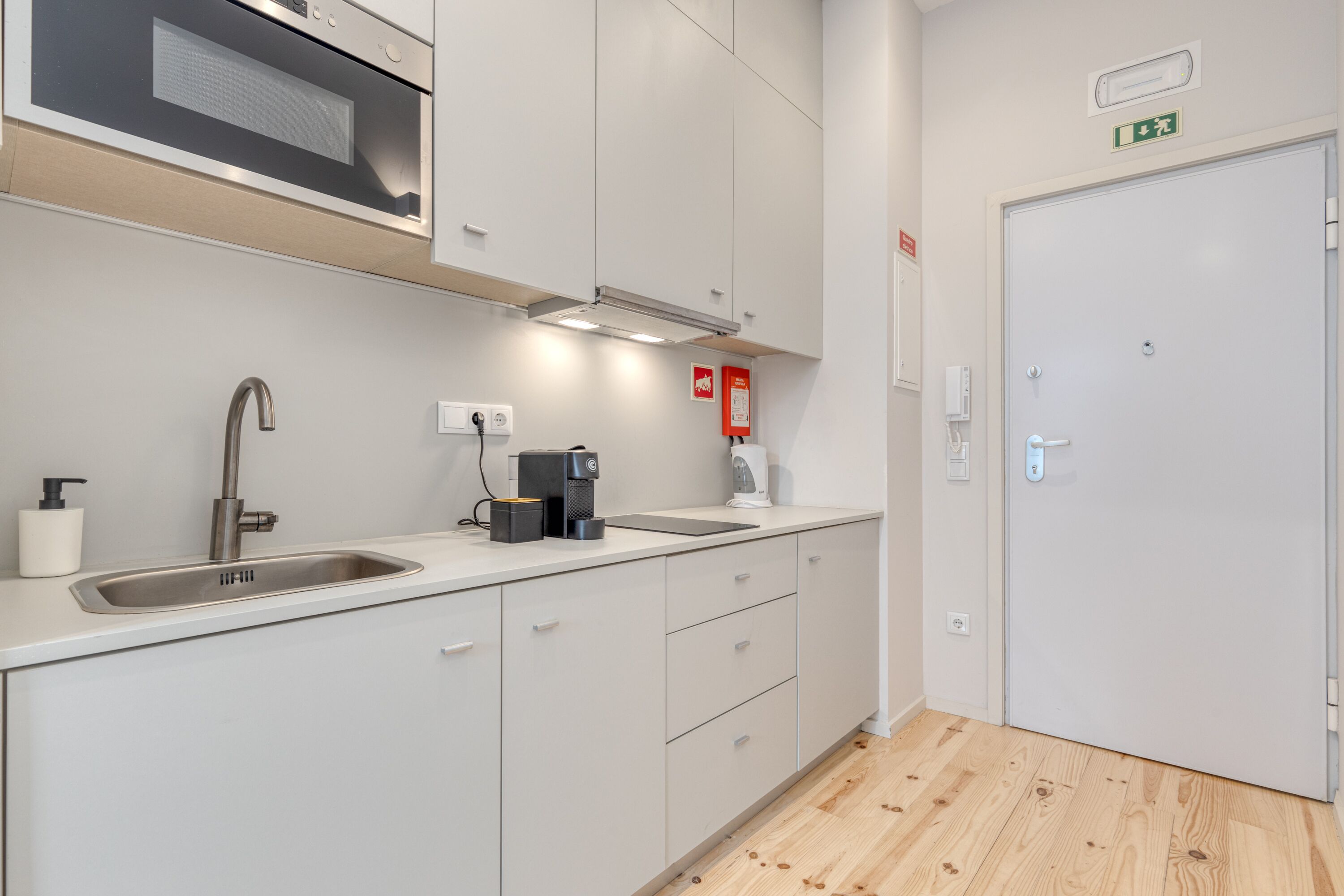 Cozinha moderna com pia de aço inoxidável, máquina de café e forno embutido.