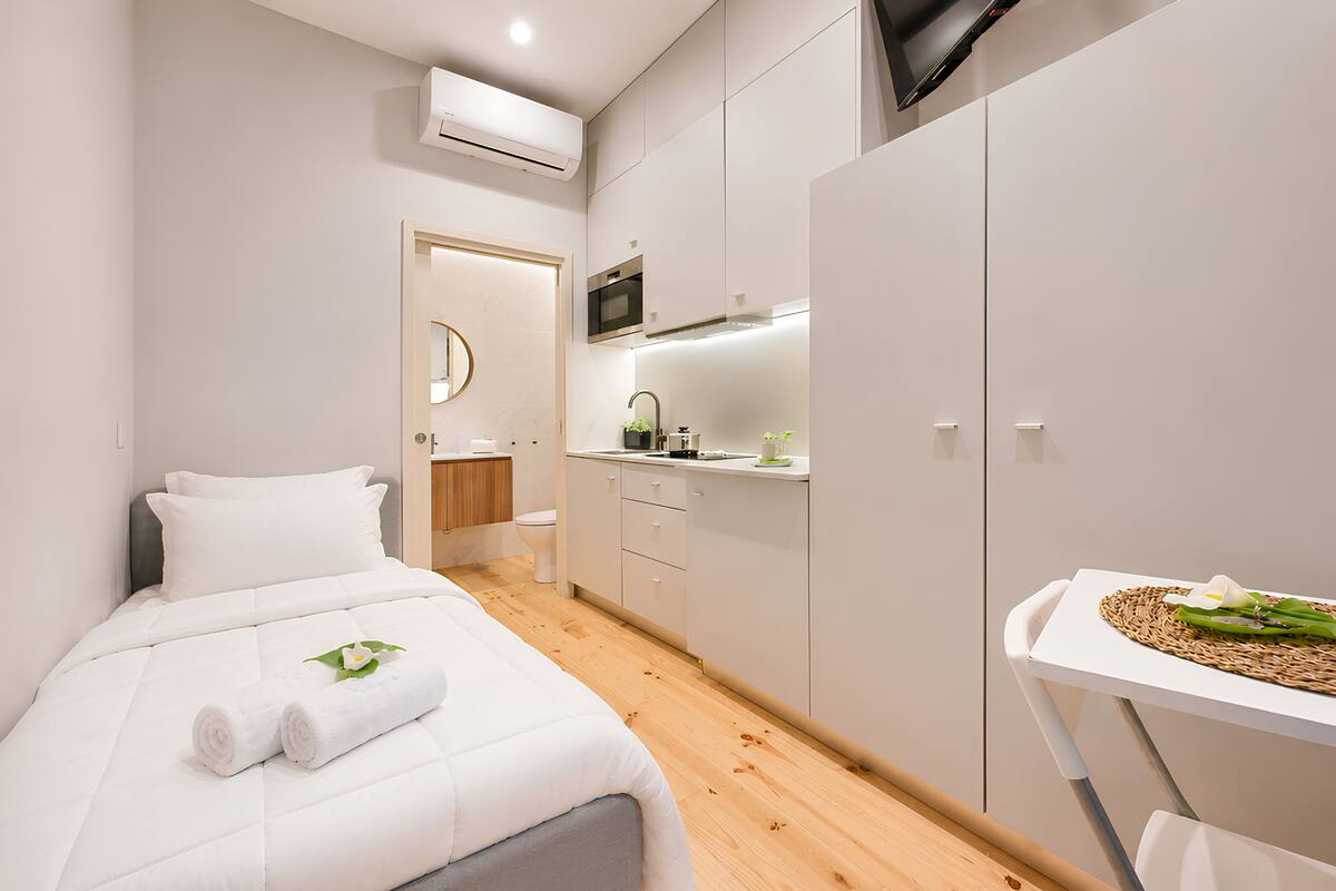 A modern hotel room with a bed, a small kitchenette, a bathroom, and a TV.