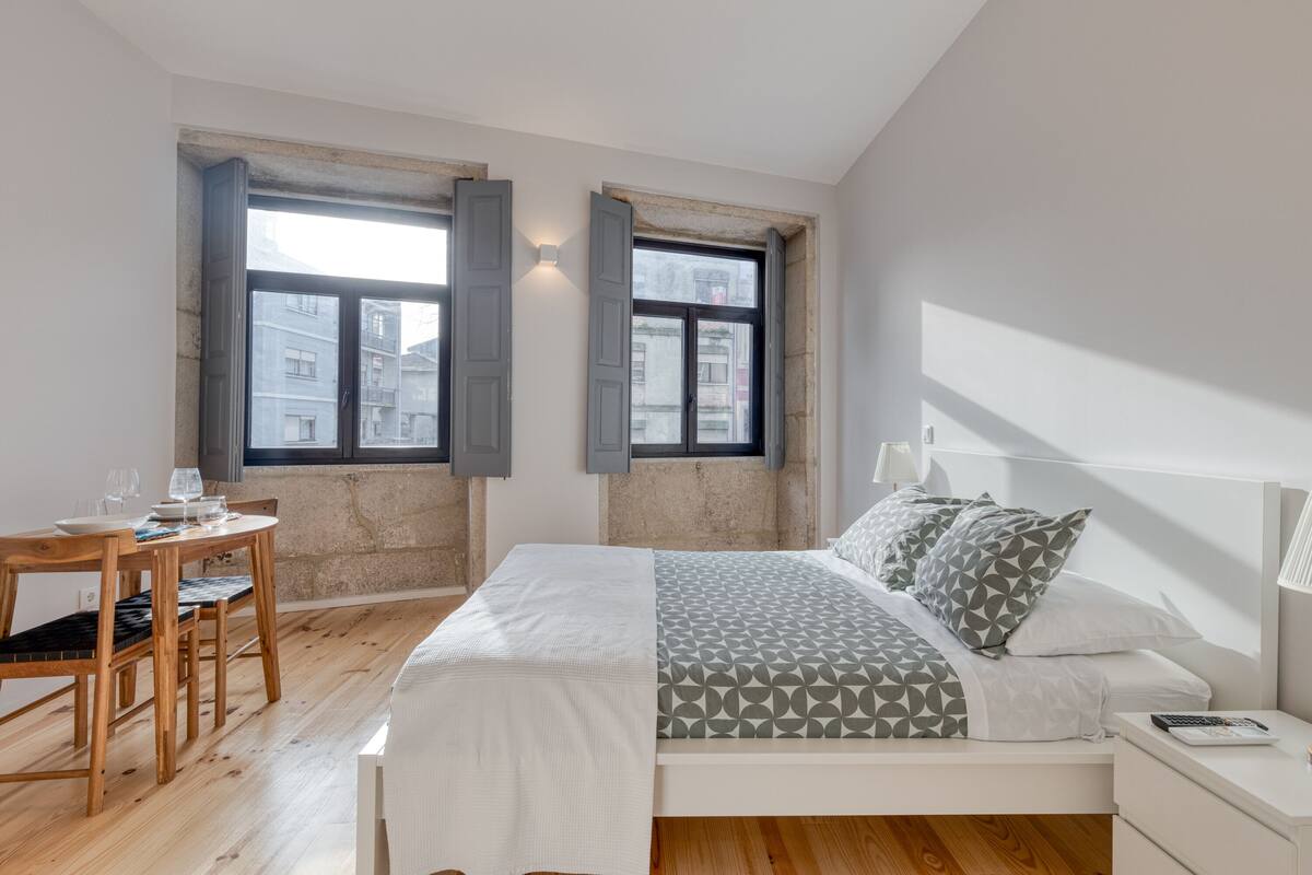 A bedroom with a bed, bedside table, lamp, and a window with shutters.