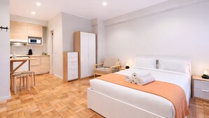 Una habitación de hotel moderna con cama, mesita de noche y una zona de kitchenette.