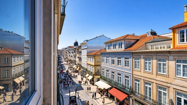Escena de calle concurrida con edificios históricos, un paseo peatonal y zonas de estar al aire libre.