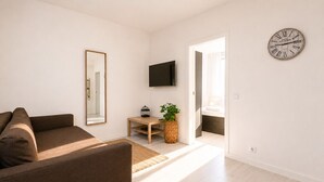 Una sala de estar moderna con un sofá marrón, una mesa de centro de madera, un televisor de pantalla plana, un espejo grande y un reloj de pared.
