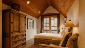 A bedroom with a wooden ceiling, a large window, a bed, a dresser, and a lamp.