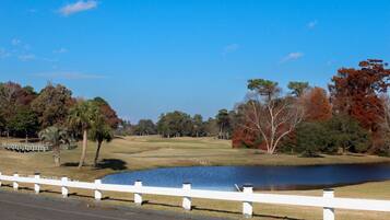 Un parcours de golf avec un étang, une clôture blanche et des arbres aux couleurs automnales.
