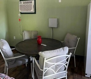 A dining area with a round table and four chairs, an air conditioning unit, and a power outlet on the wall. - The Juniper ~ Cabin Fourteen ~ Pet Friendly ~ Lakefront (Royal)